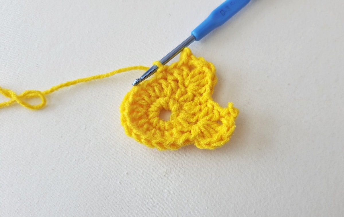 Maple Leaf Crochet Pattern Step 12 A yellow crocheted flower with a blue crochet hook.