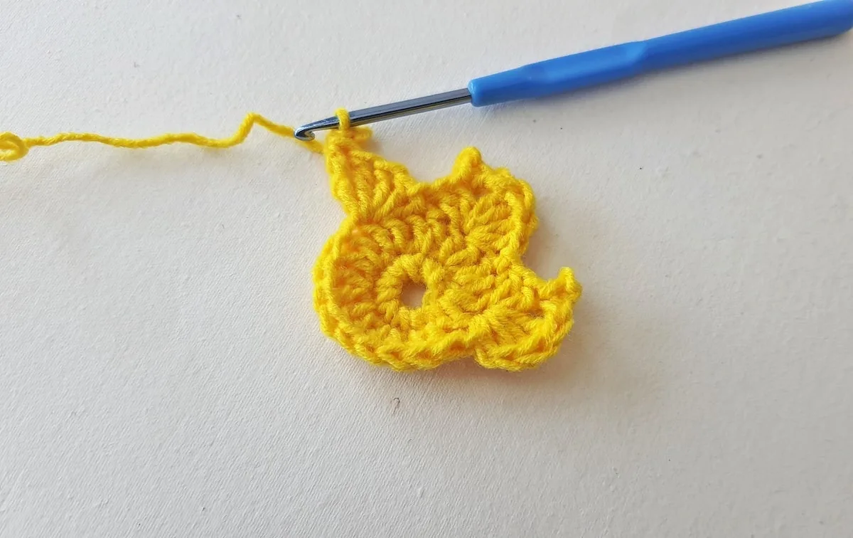 Maple Leaf Crochet Pattern Step 13 A yellow crocheted flower with a blue crochet hook.