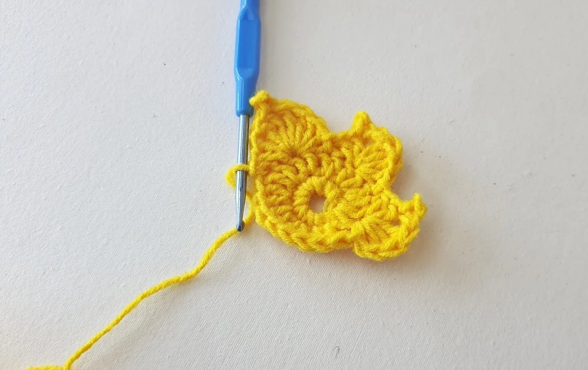 Maple Leaf Crochet Pattern Step 14 A yellow crocheted flower with a blue crochet hook.
