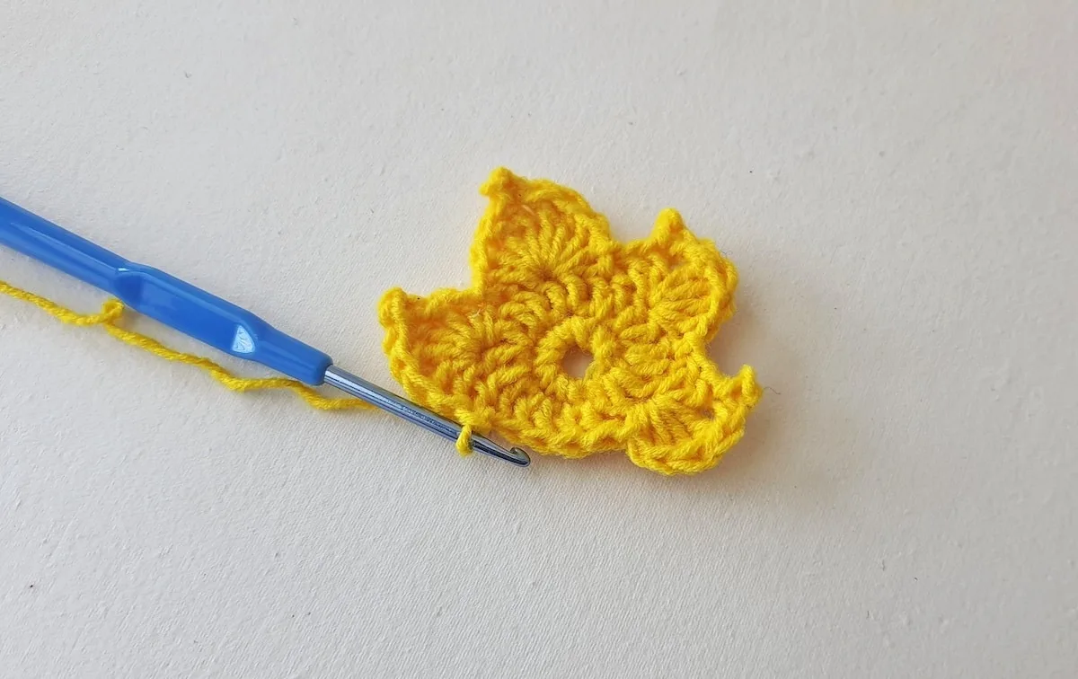 Maple Leaf Crochet Pattern Step 16 A yellow crocheted flower with a blue crochet hook.