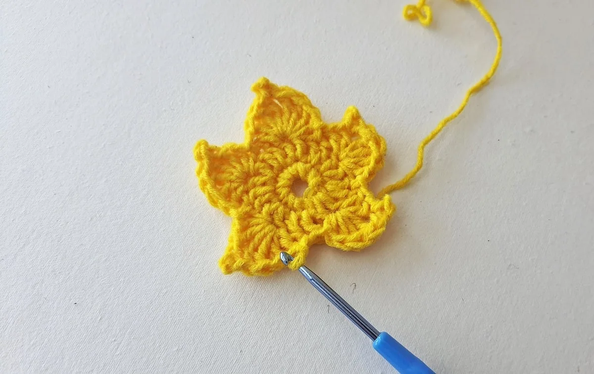 Maple Leaf Crochet Pattern Step 17 A yellow crocheted flower with a blue crochet hook.