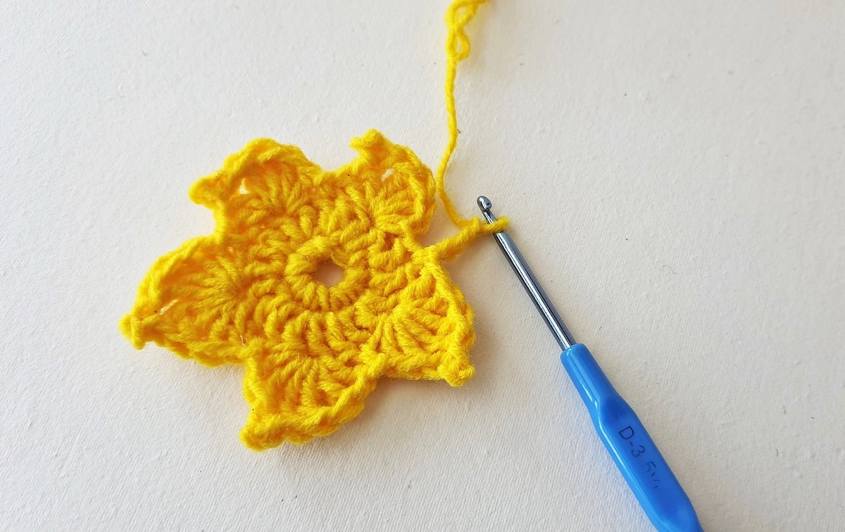 Maple Leaf Crochet Pattern Step 18 A yellow crocheted flower with a blue crochet hook.