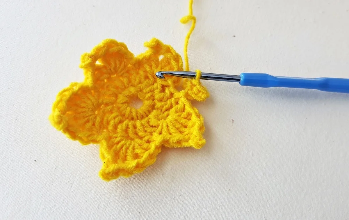 Maple Leaf Crochet Pattern Step 19 A yellow crocheted flower with a blue crochet hook.