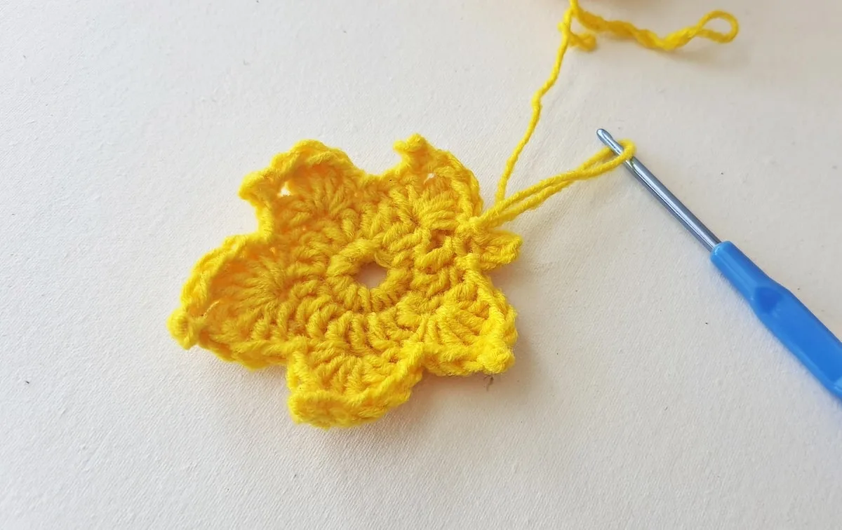 Maple Leaf Crochet Pattern Step 20 A yellow crochet flower with a blue crochet hook.