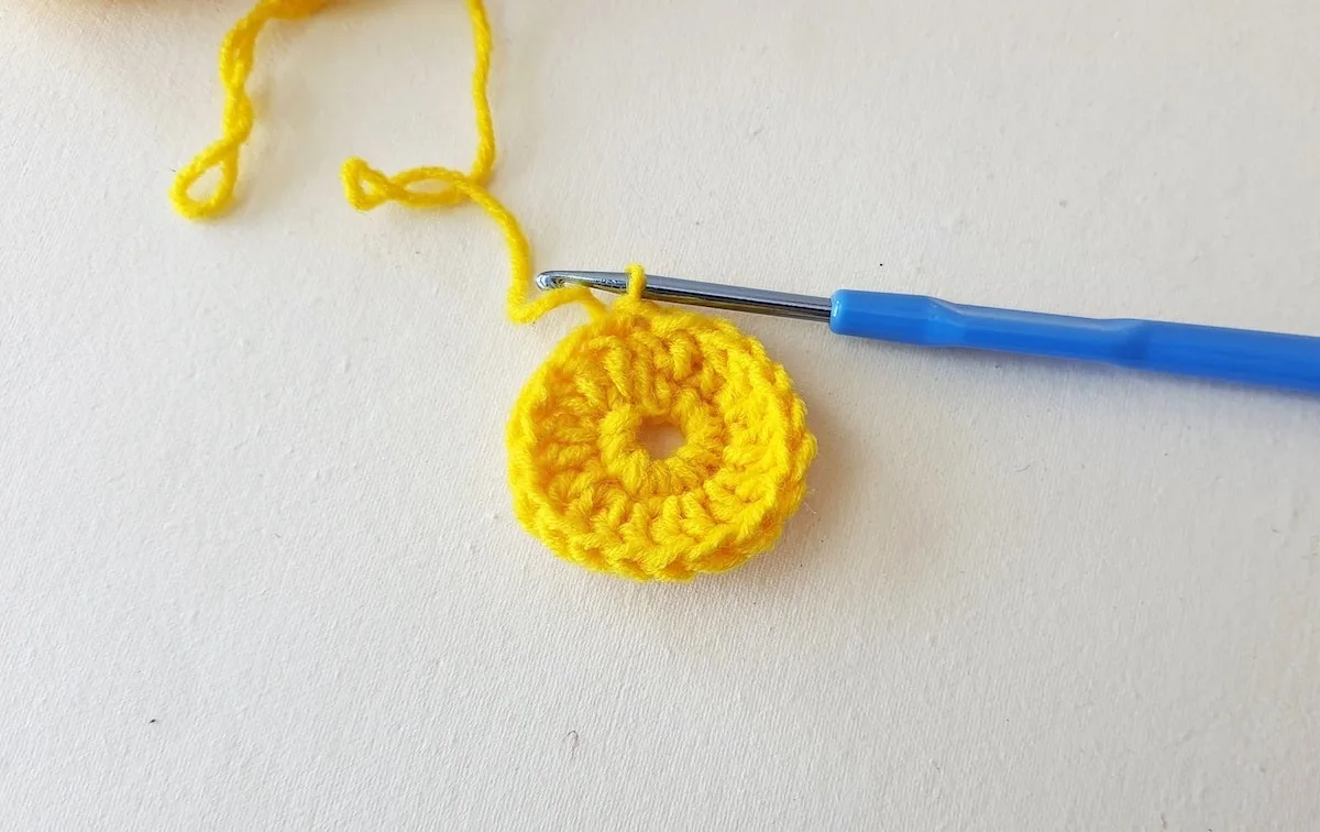 Maple Leaf Crochet Pattern Step 6 A yellow crocheted flower with a blue crochet hook.