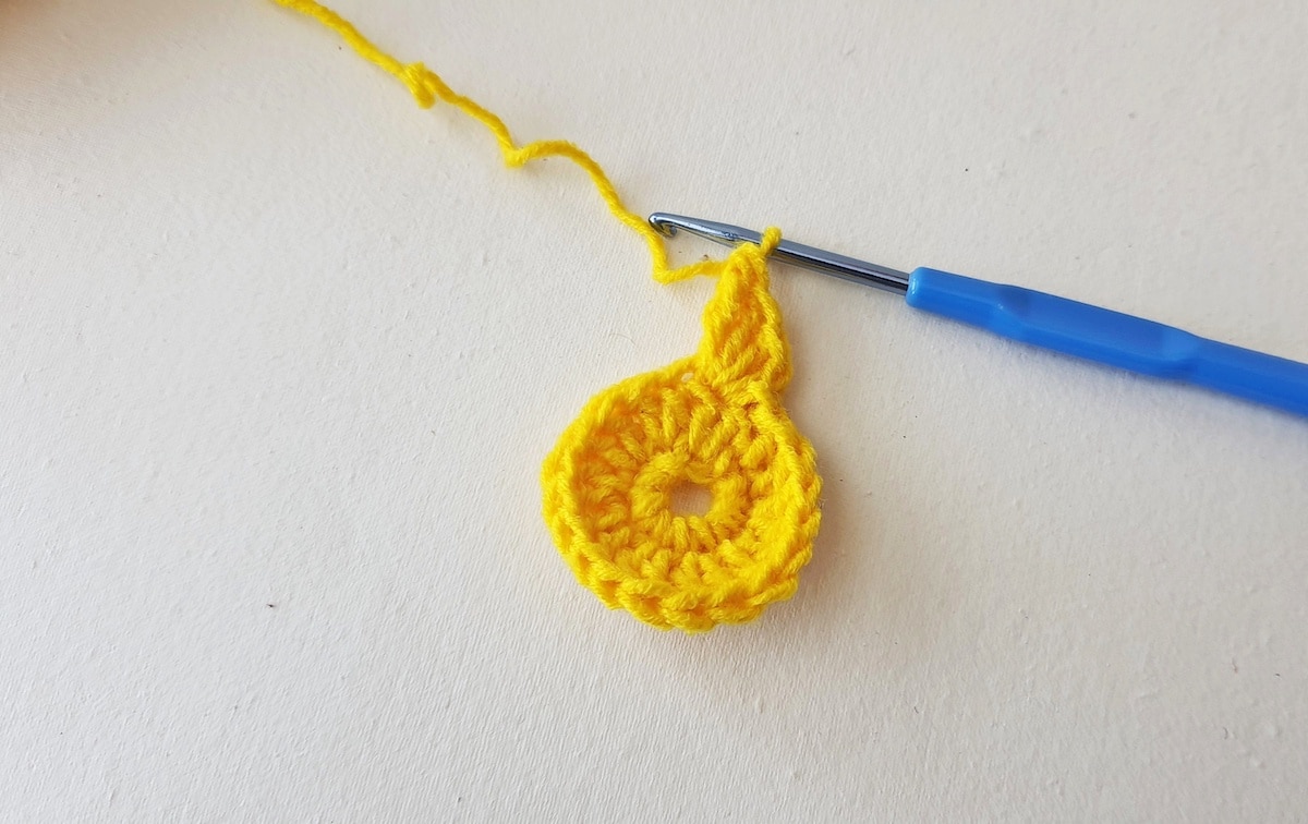 Maple Leaf Crochet Pattern Step 8 A yellow crocheted flower with a blue crochet hook.