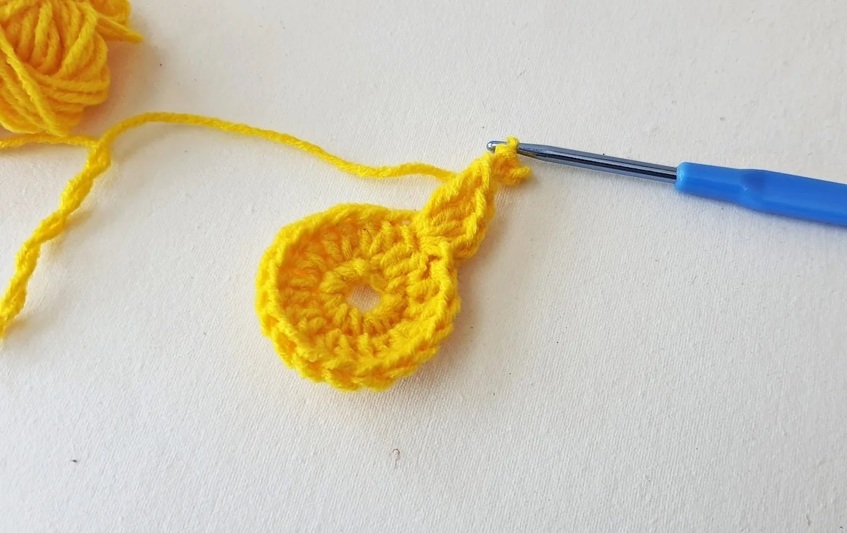 Maple Leaf Crochet Pattern Step 9 A yellow crocheted ball with a blue crochet hook.