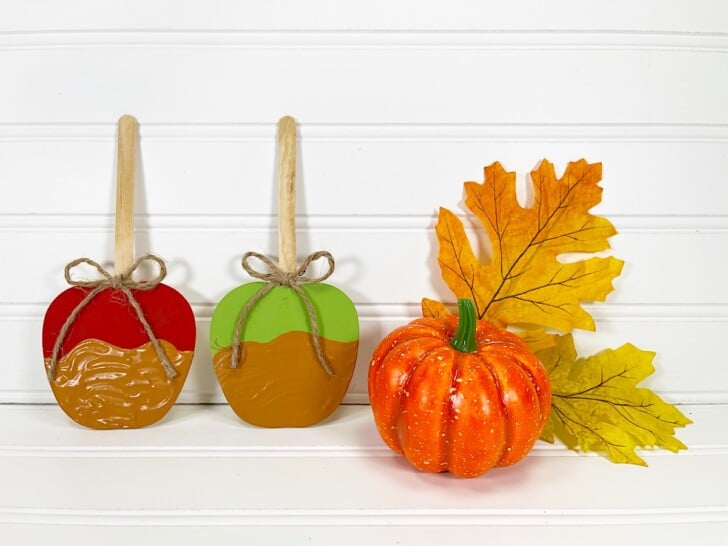 Candy Apple Craft with Two pumpkins and a leaf on a white table.