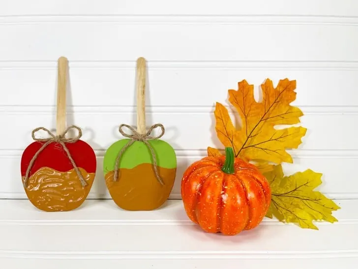 Candy Apple Craft with Two pumpkins and a leaf on a white table.