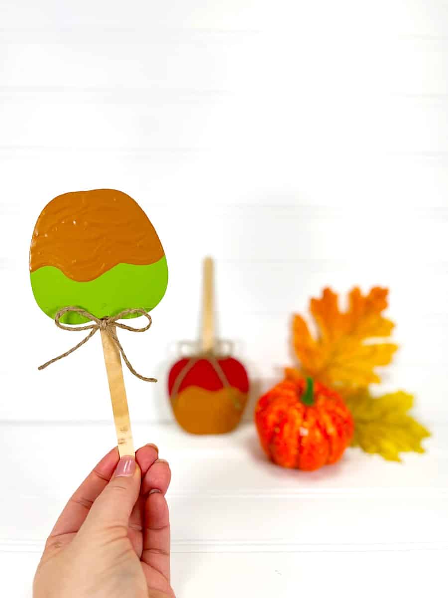 A hand holding a Candy Apple Craft popsicle stick with a pumpkin on it.
