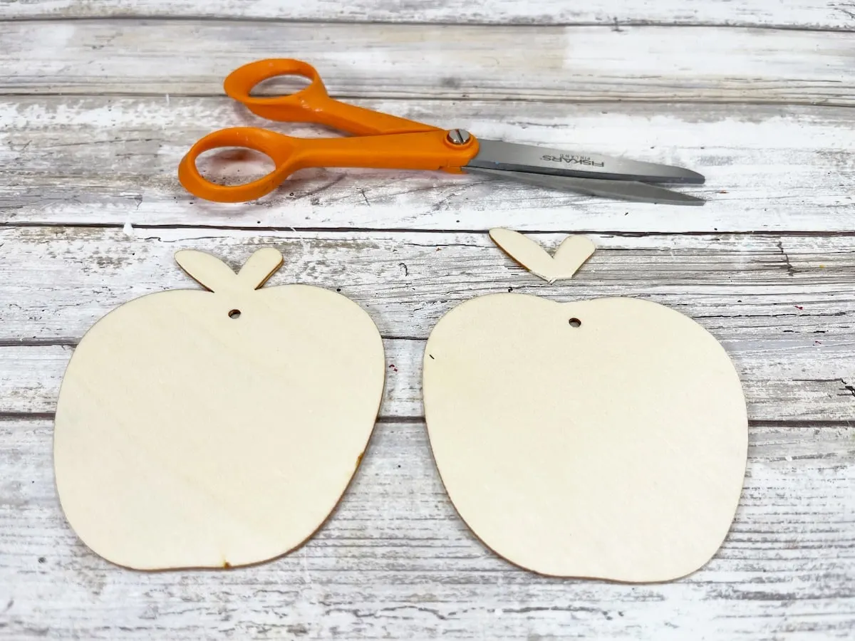 Candy Apple Craft Step 1 A pair of scissors next to two wooden apple ornaments.