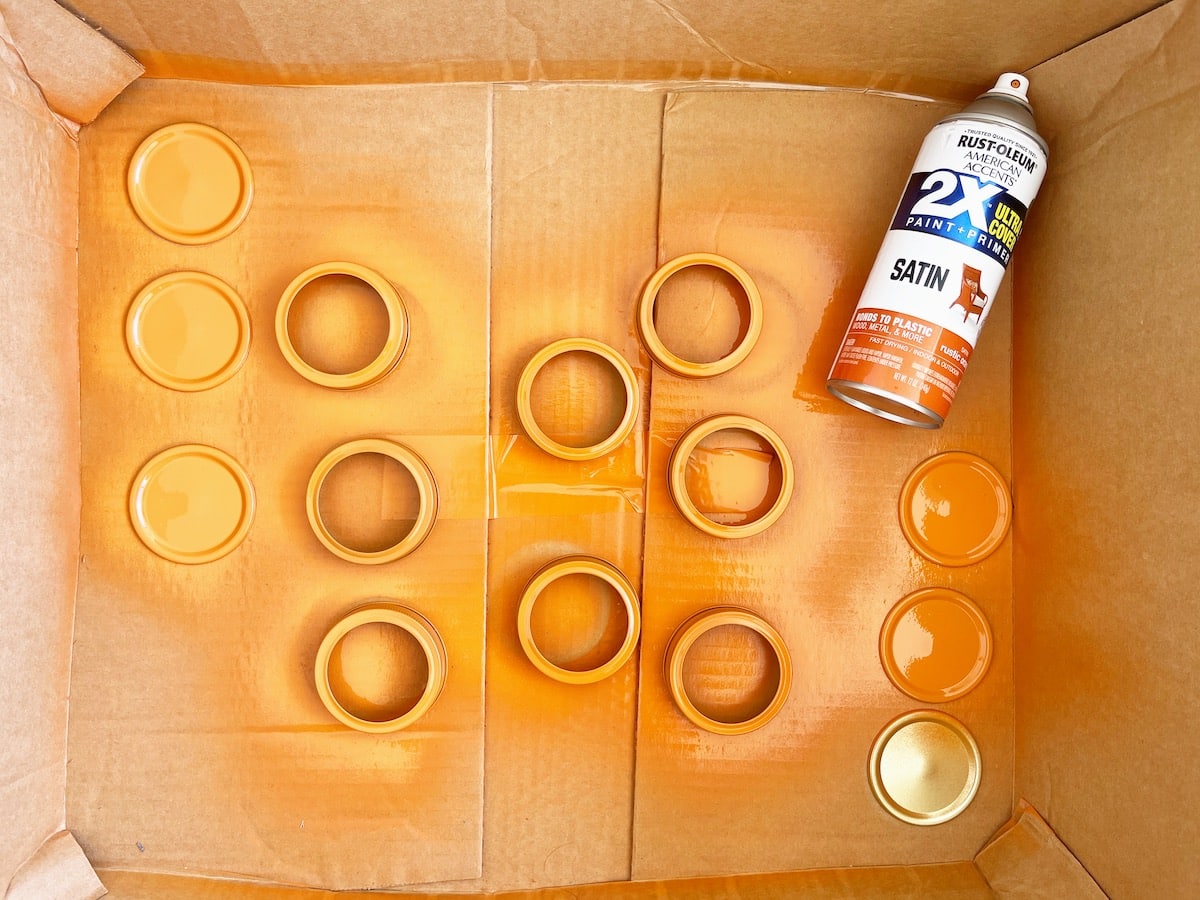 Canning Lid Pumpkins Step 1 with orange spray paint in a cardboard box