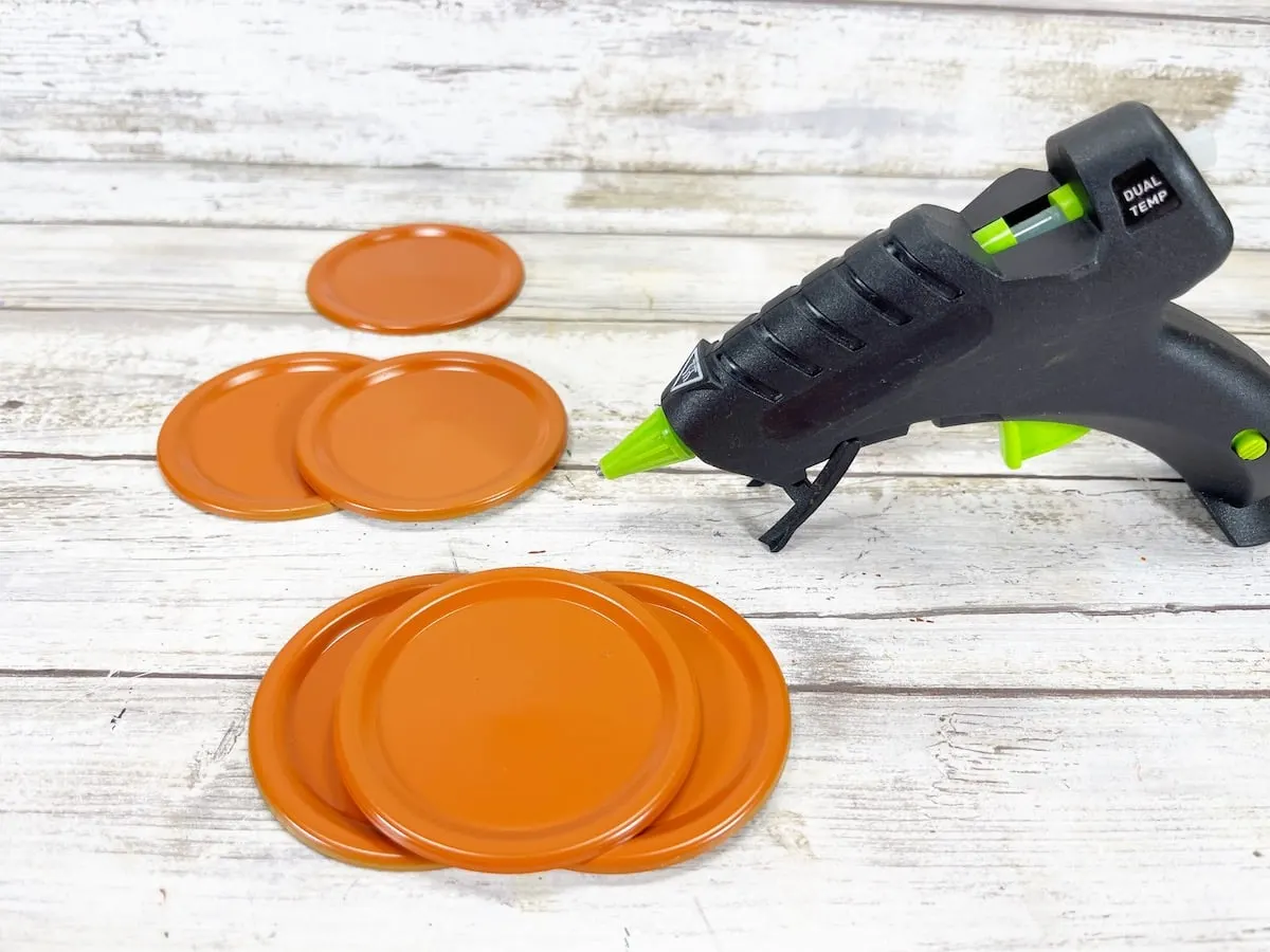 Canning Lid Pumpkins Step 3 with orange lids and hot glue gun on white background