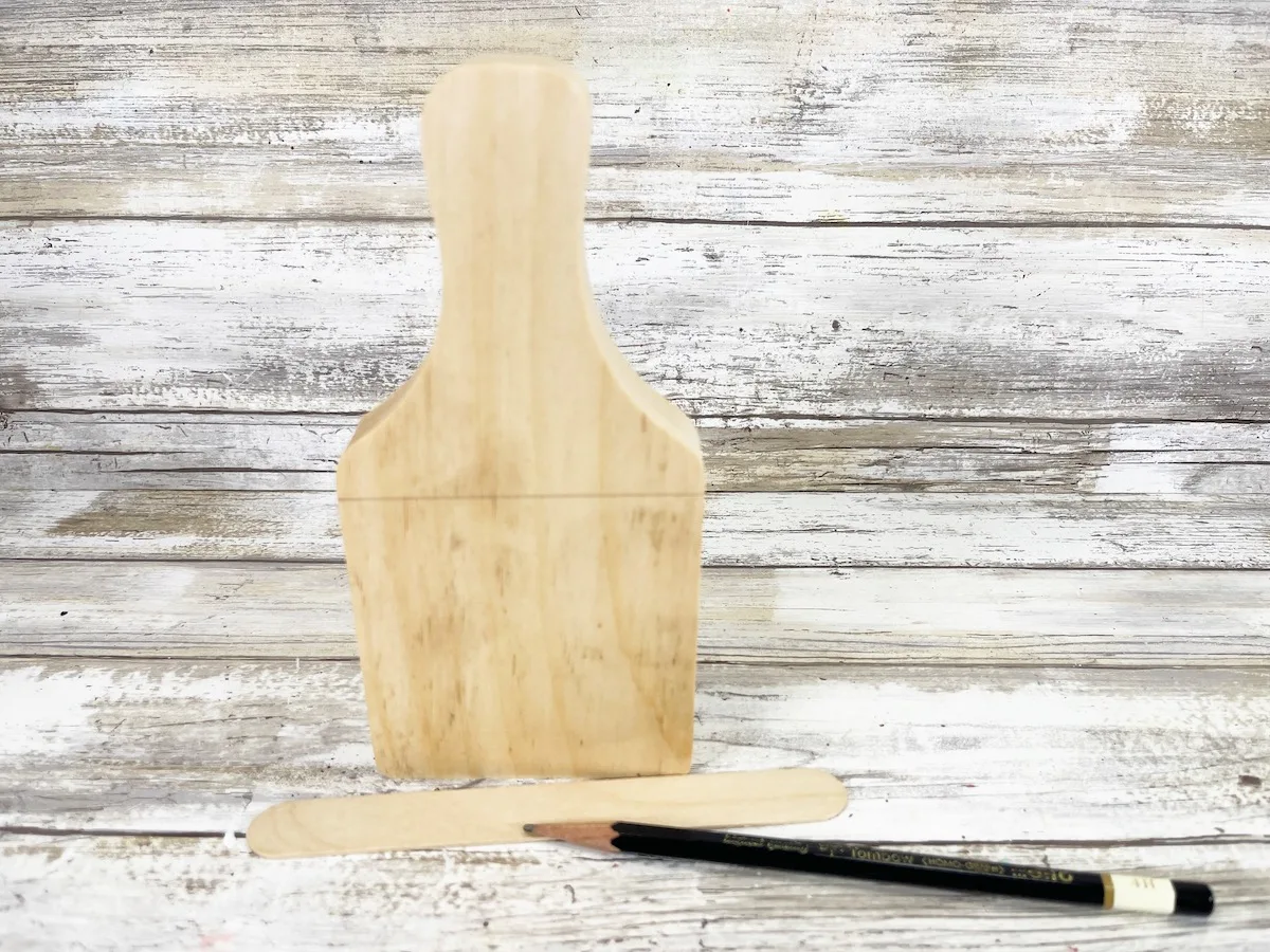 Cutting Board Scarecrow Step 1 A wooden bottle opener with a pencil next to it.