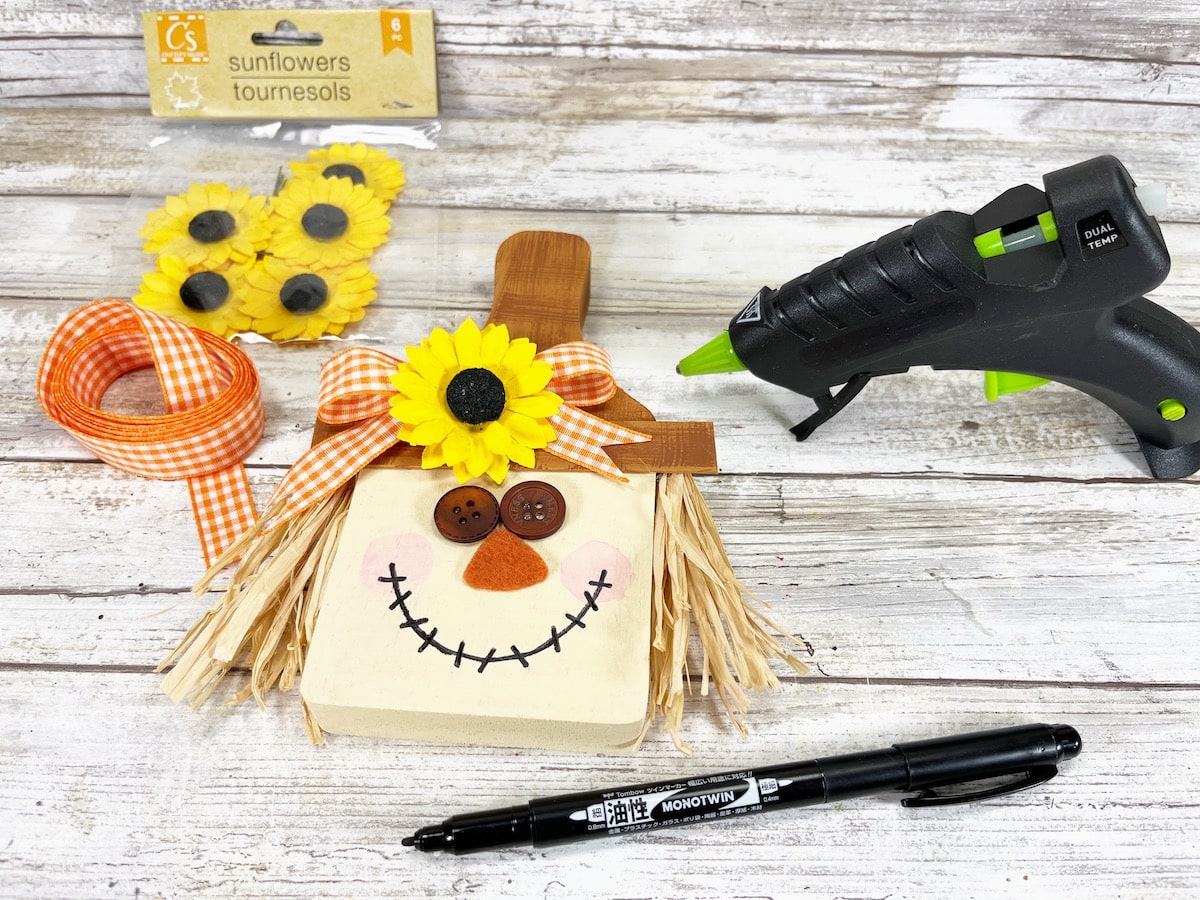 Cutting Board Scarecrow Step 10 kit with a glue gun and sunflowers.