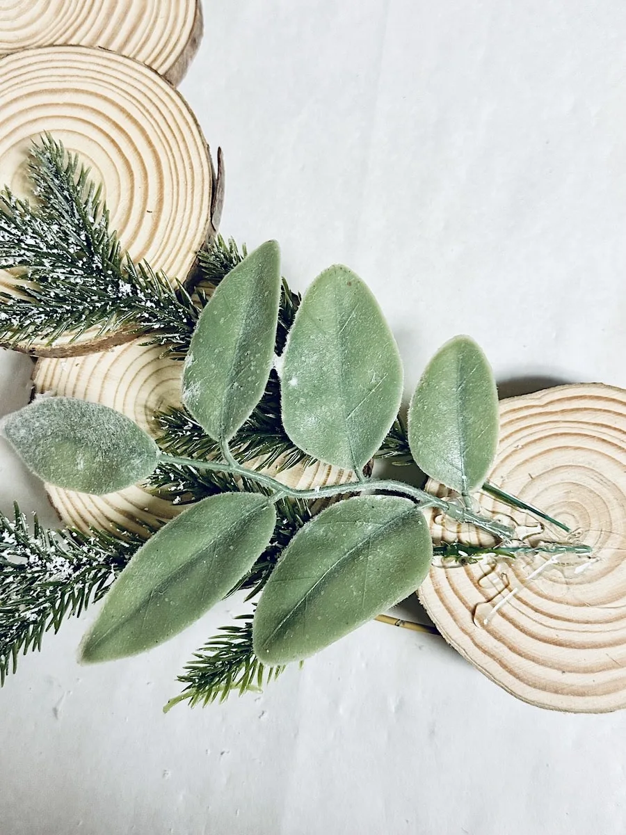 Wood Slice Wreath Step 6 faux green leaves and pine hot glued to wood slices