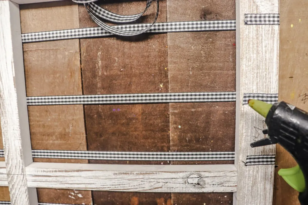 A woman is using a glue gun on a wooden frame.