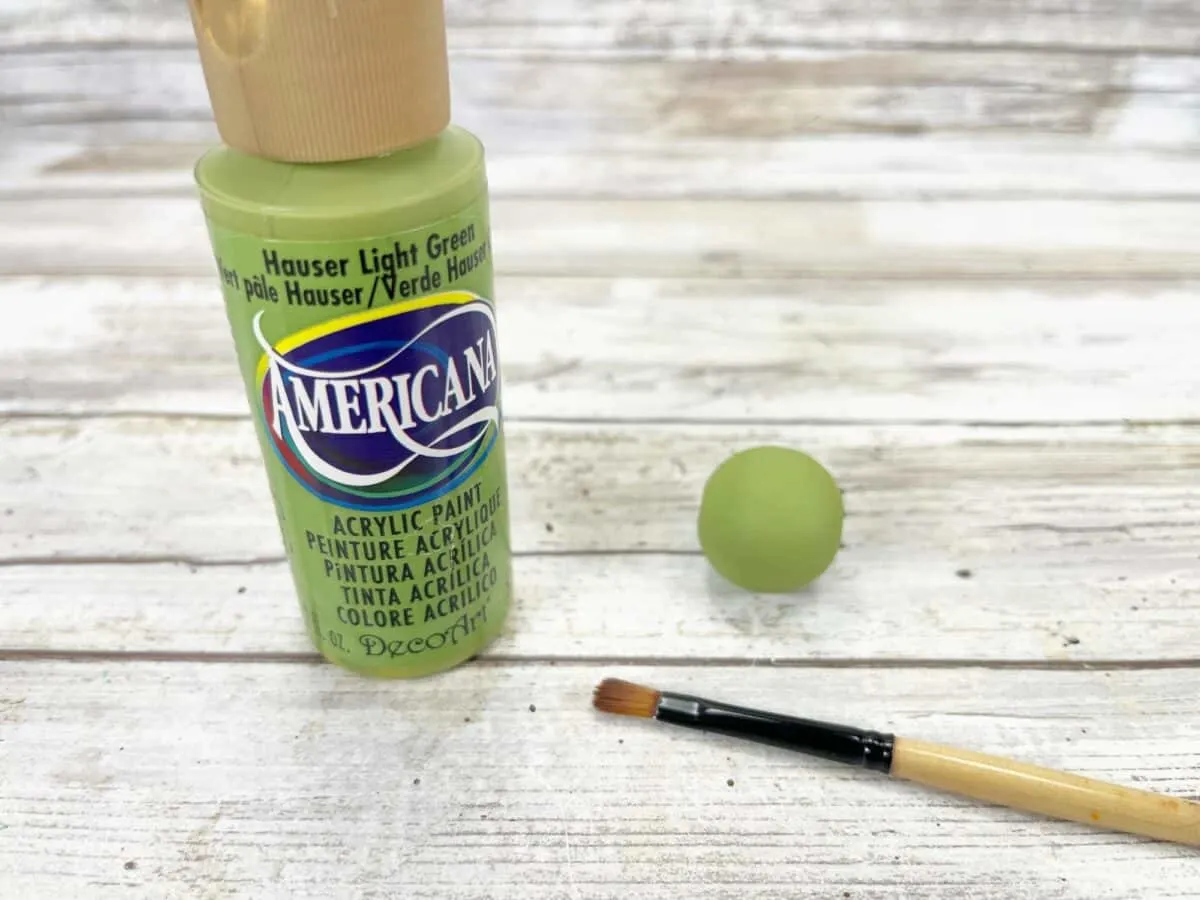 A bottle of green paint with a brush next to it.