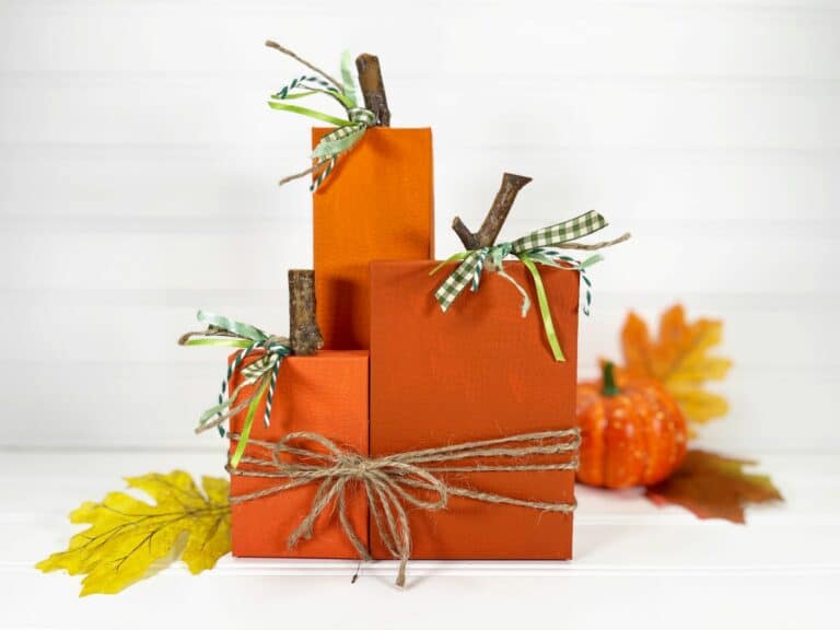 Three orange box pumpkins sitting on top of a wooden table.
