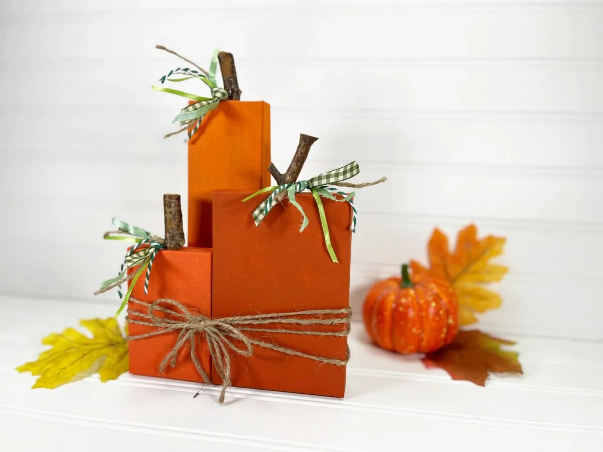 Three orange pumpkins on a table with leaves and twine.