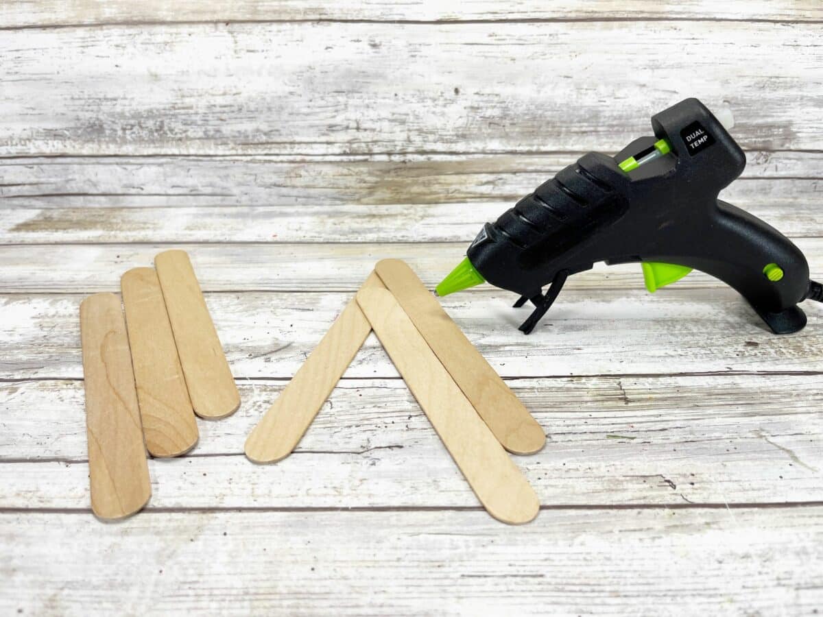Glue gun and popsicle sticks on a wooden table.