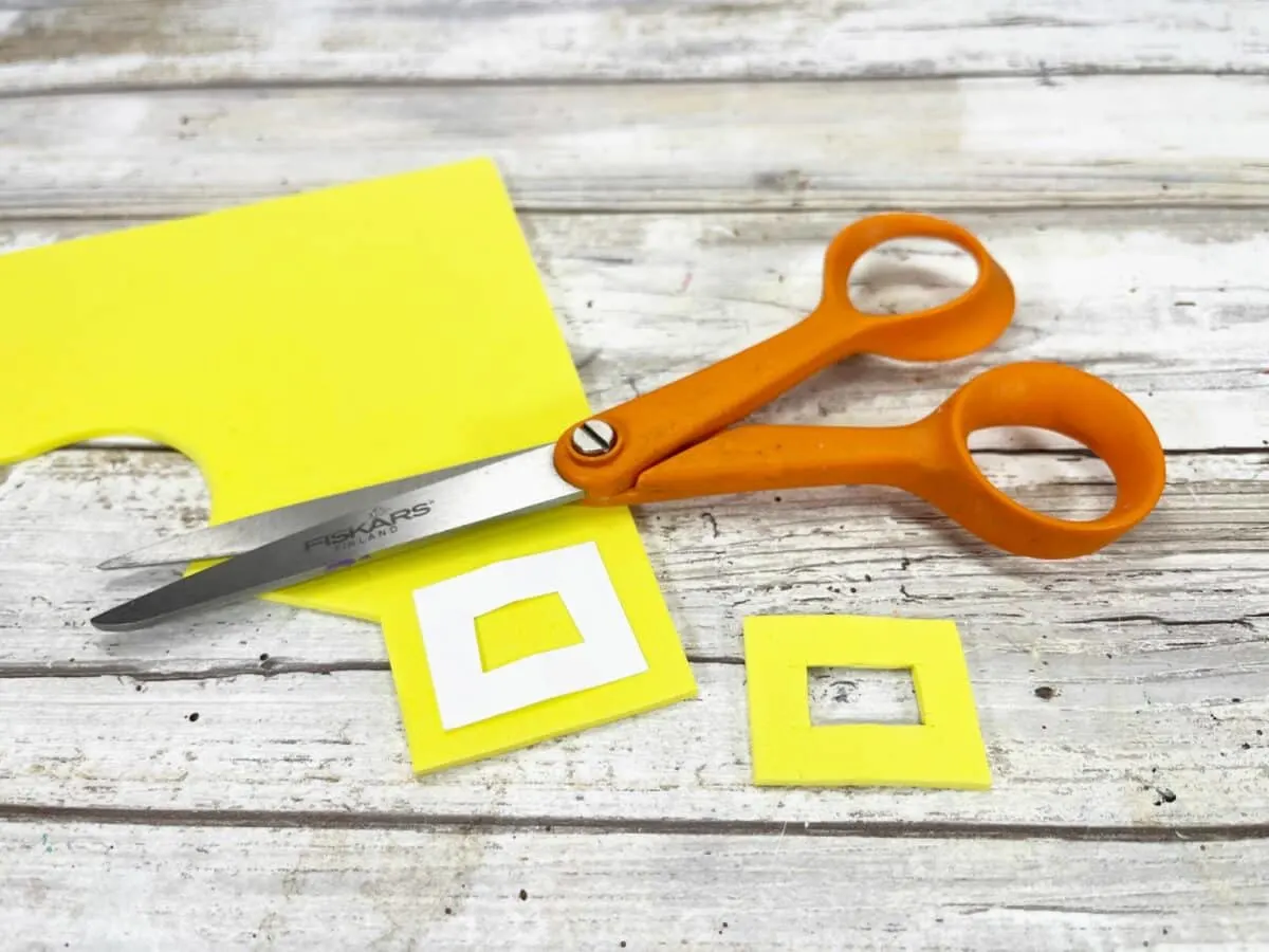 A pair of scissors next to a yellow piece of paper.