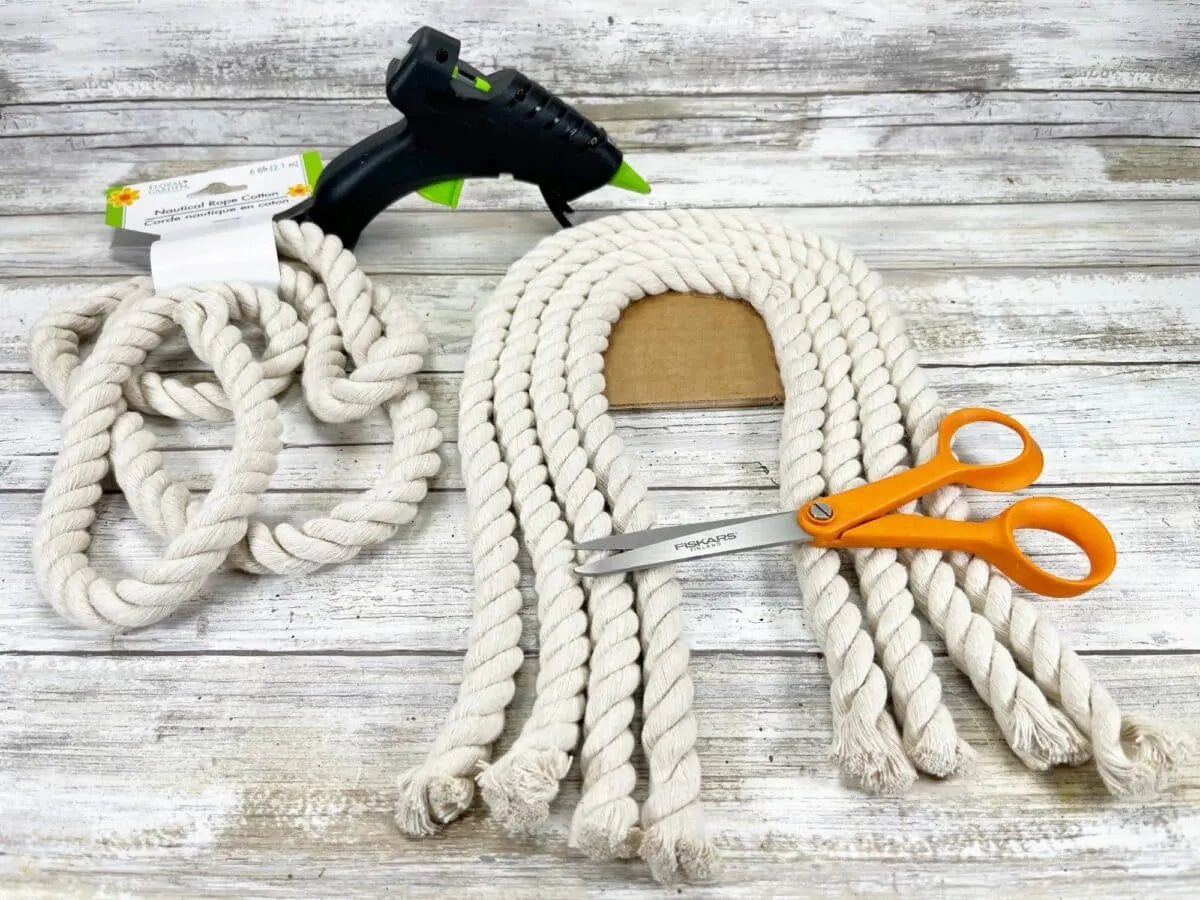A pair of scissors and a glue gun next to a rope.