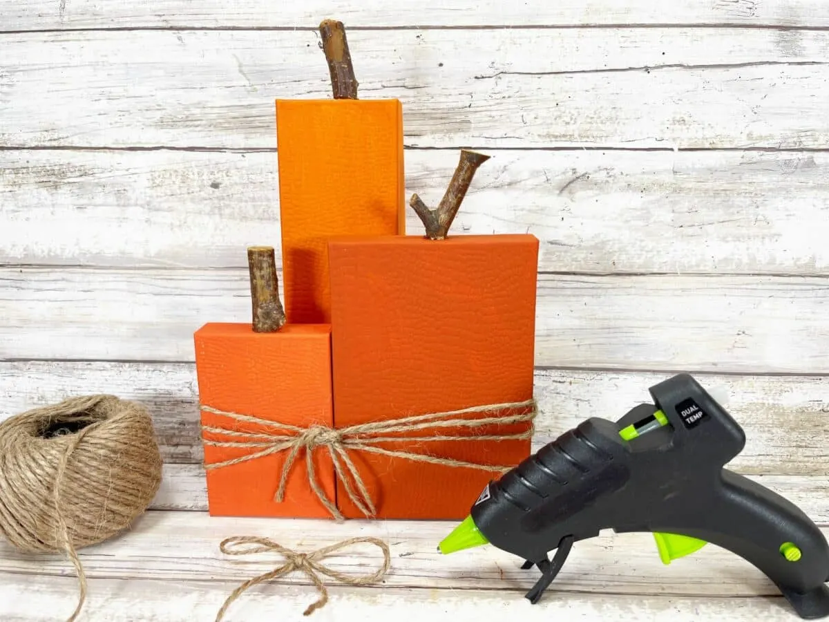 A pair of orange pumpkins and a glue gun on a wooden table.