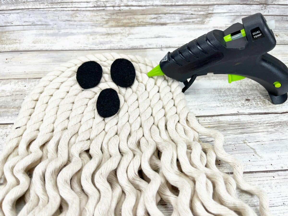 A knitted ghost with a glue gun on a wooden surface.