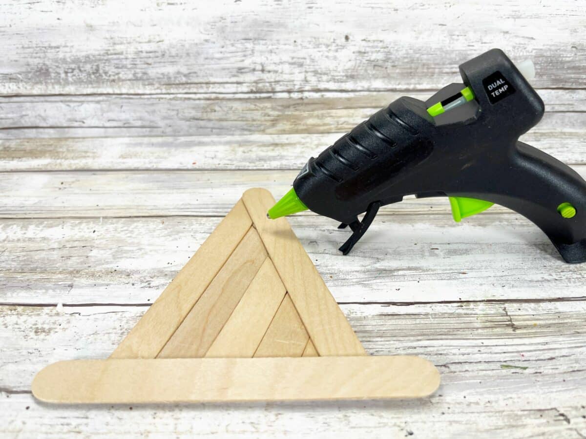 A glue gun on top of a wooden triangle.