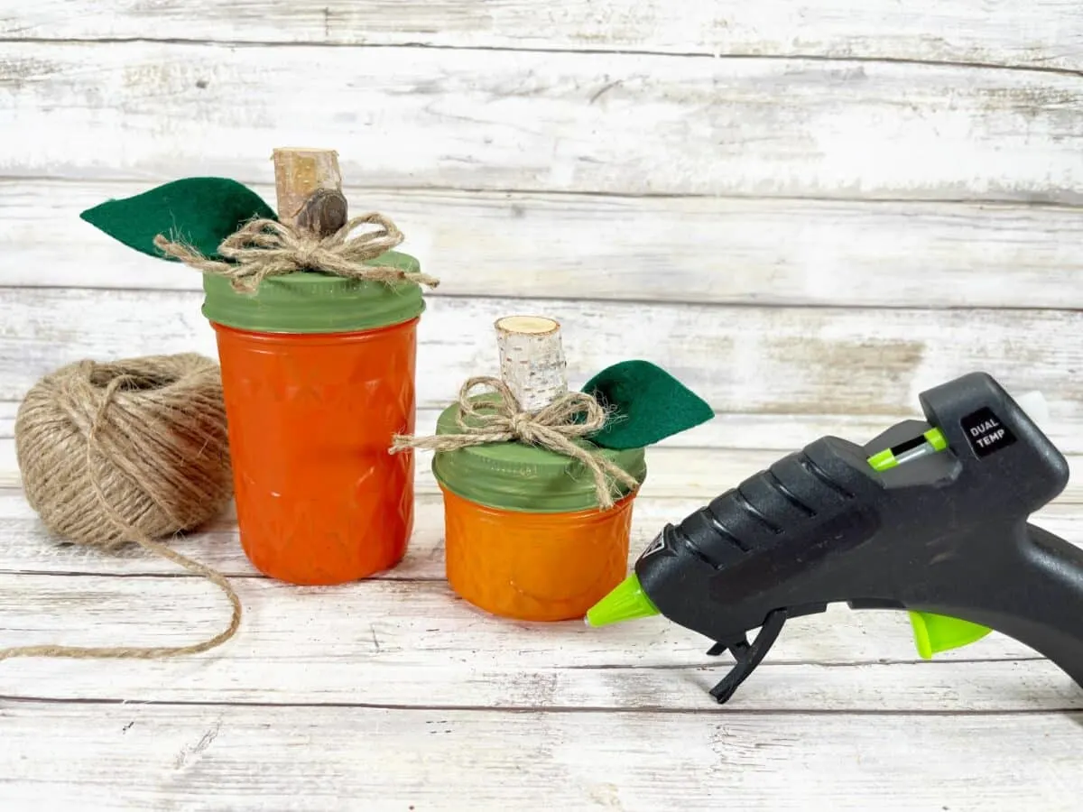 A pair of mason jars and a glue gun on a wooden table.