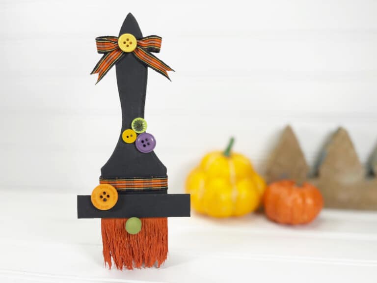 A witch broom on a table with pumpkins and buttons.