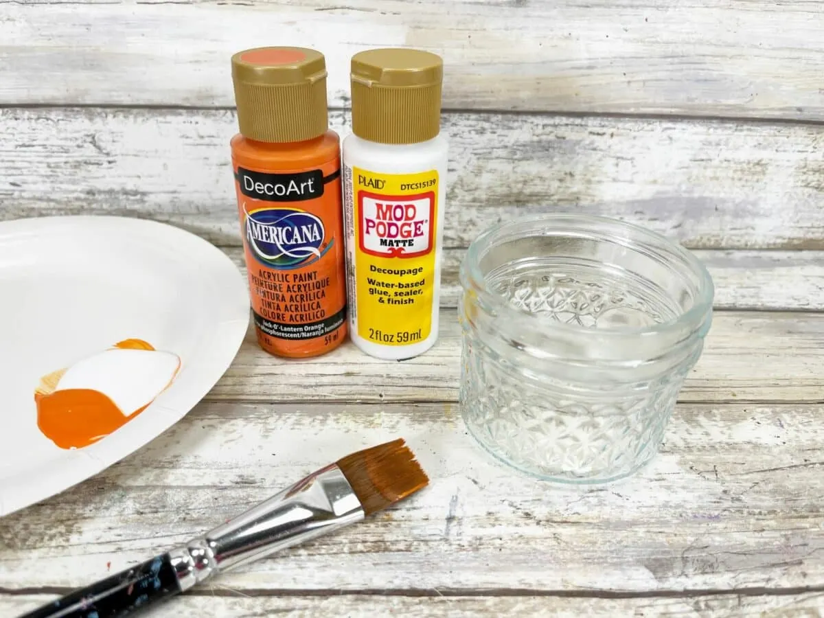A plate with paint, paintbrush, and a jar of paint.