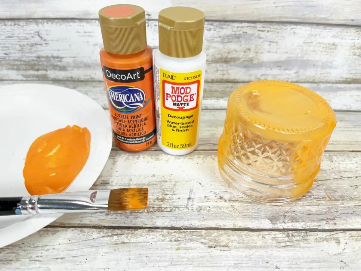 A plate with orange paint and a brush next to it.