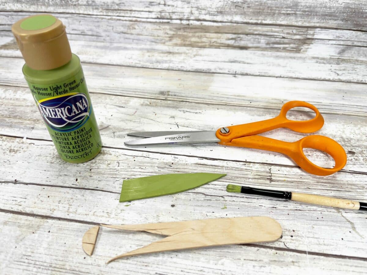 Green paint, scissors, and a bottle of paint on a wooden table.