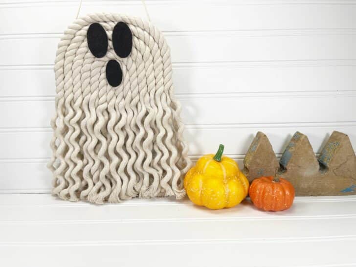 A rope ghost hanging on a wall next to pumpkins.