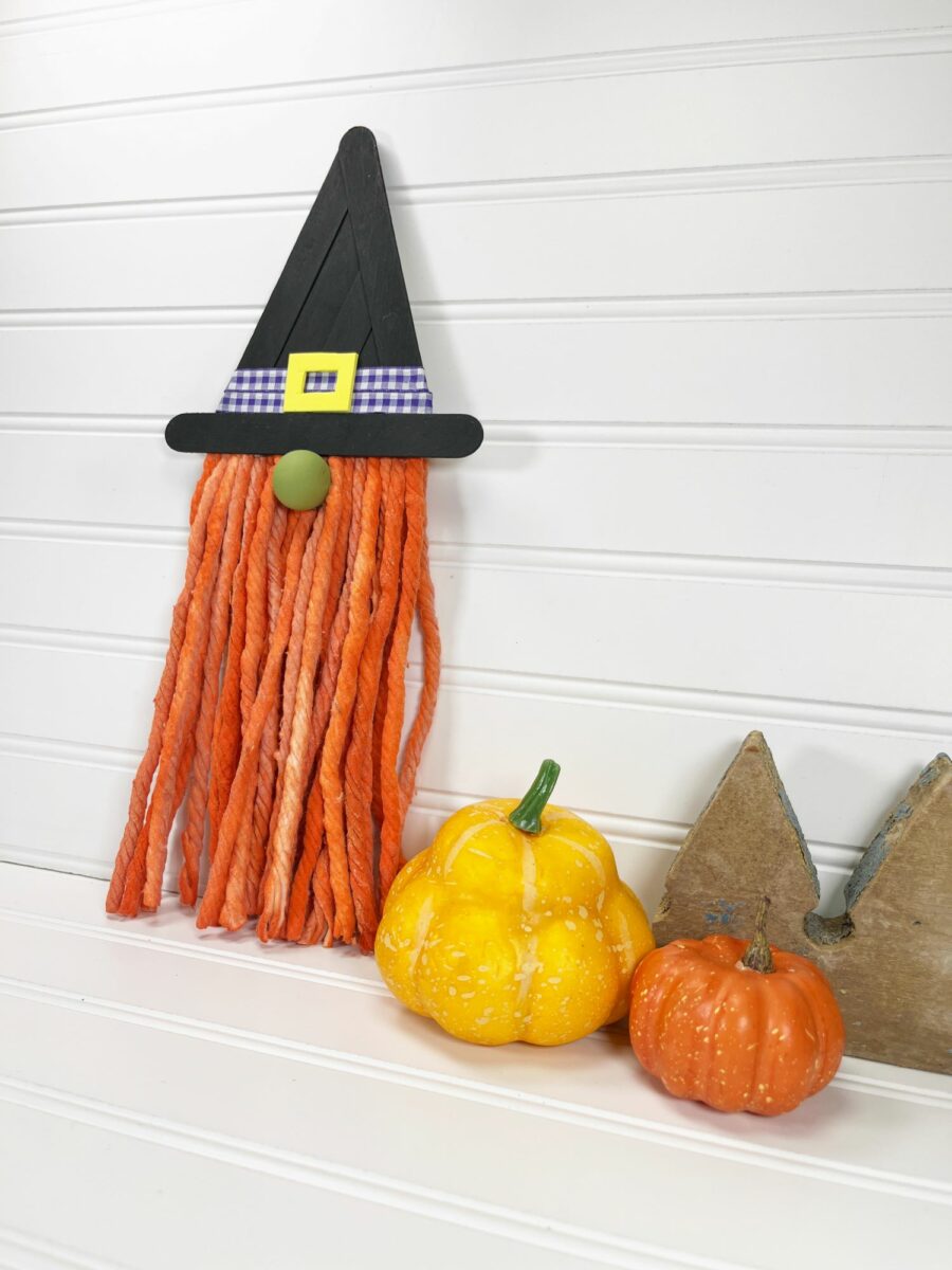 A witch hat hanging on a wall next to pumpkins.
