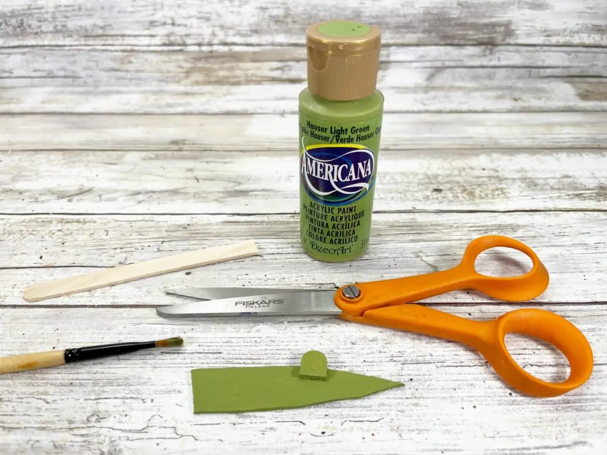 A pair of scissors, paint, and a bottle of green paint.