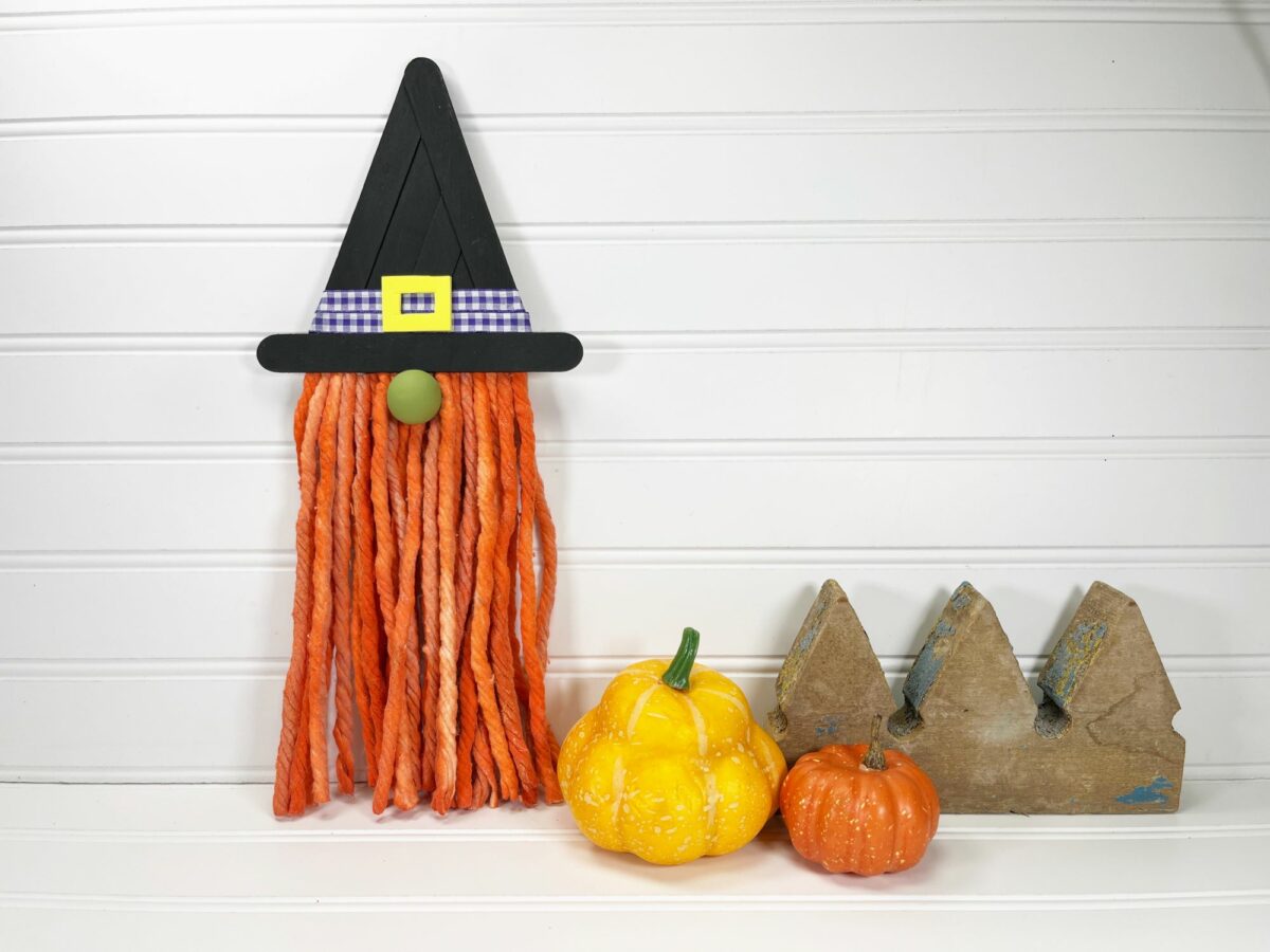 A witch hat hanging on a wall next to pumpkins.