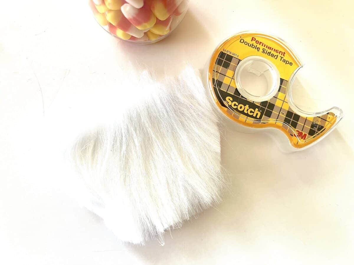 Scotch tape and white fur next to a candy jar with candy corn.