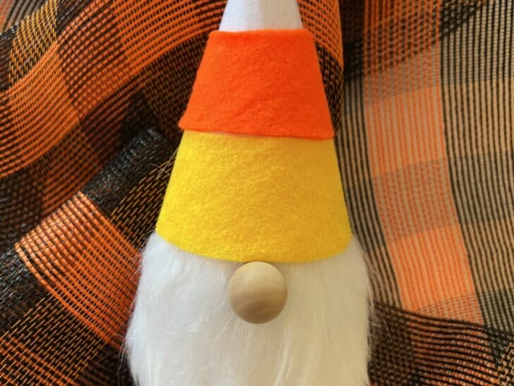A candy corn gnome on a orange and black check tablecloth.