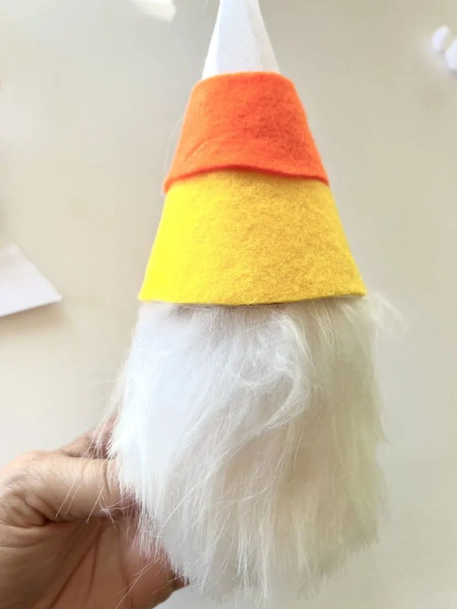 A person is holding up a candy corn gnome hat.