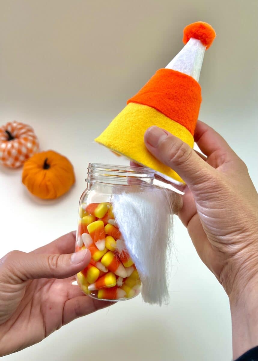 A person holding a candy corn gnome in a jar.