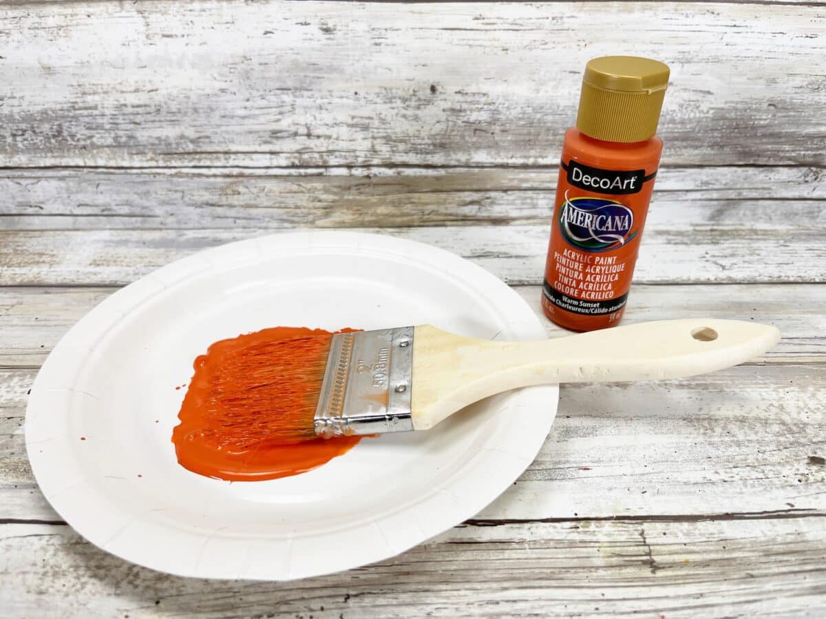 Orange paint on a plate next to a brush.