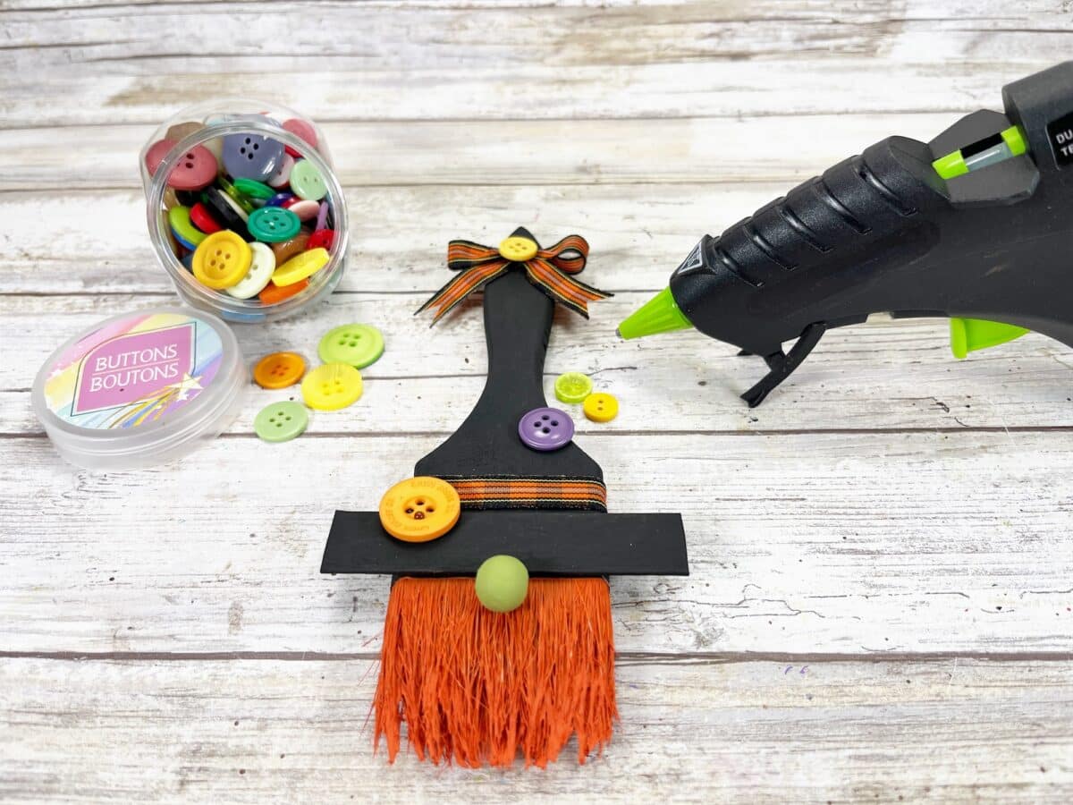 A witch's broom with a glue gun and buttons.