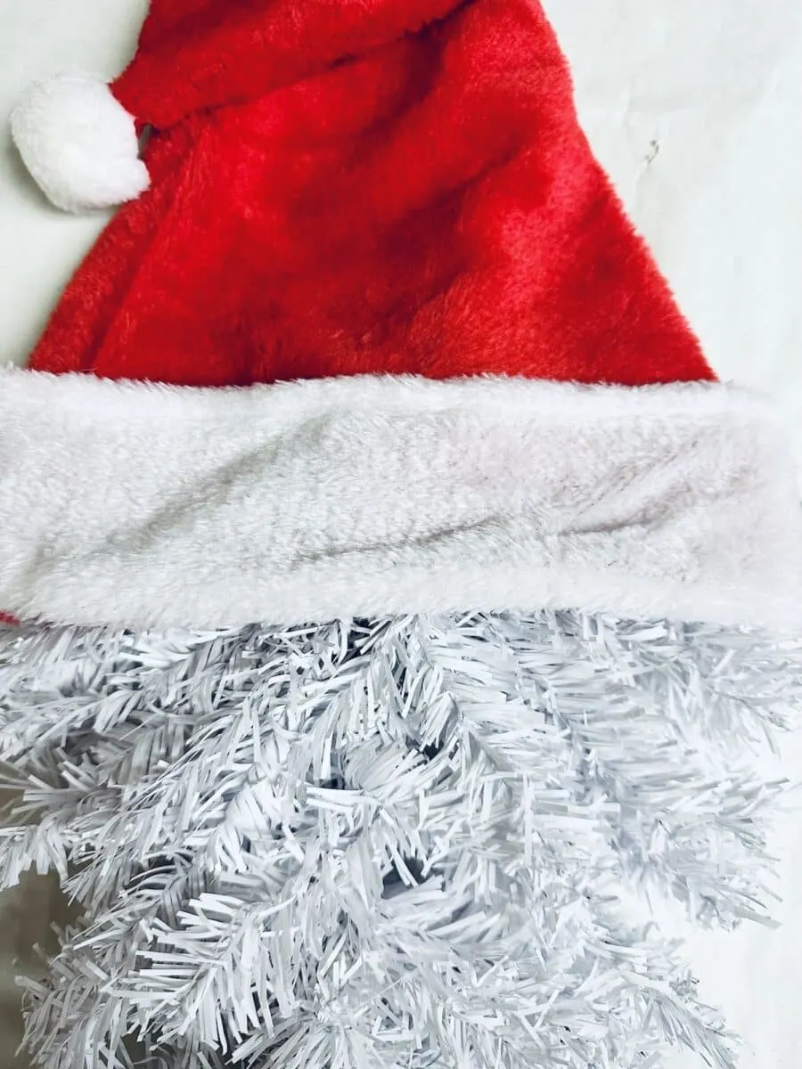 A Santa Claus hat on top of a Christmas tree with a wreath.