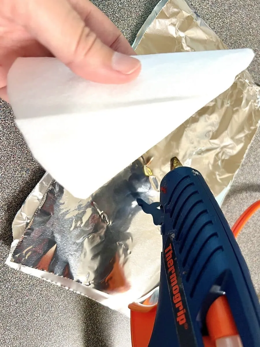 A person using a glue gun on a piece of foil.