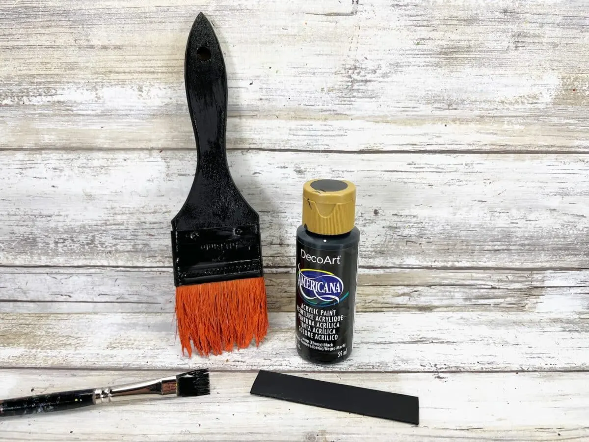 A black paint brush and orange paint brush on a wooden table.