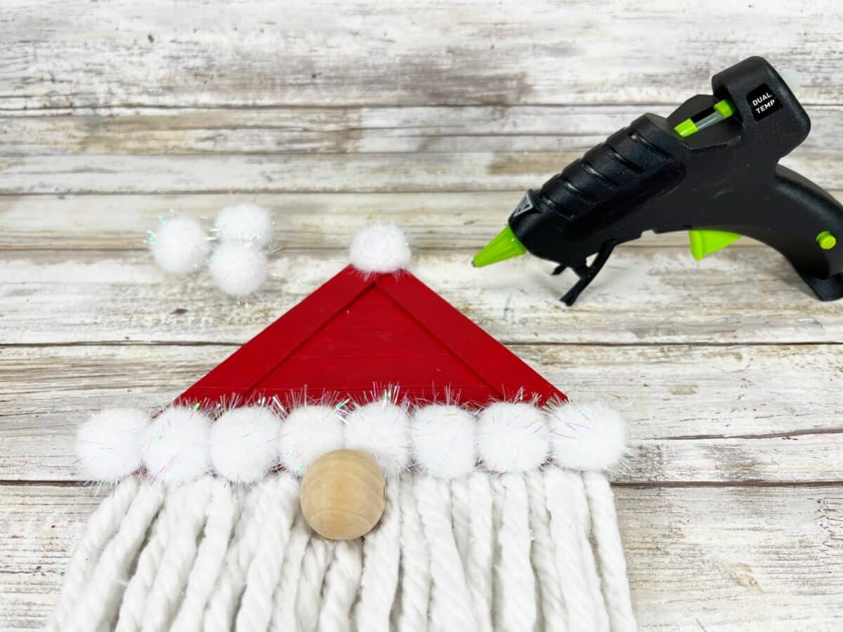 A santa claus wreath with pom poms and a glue gun.