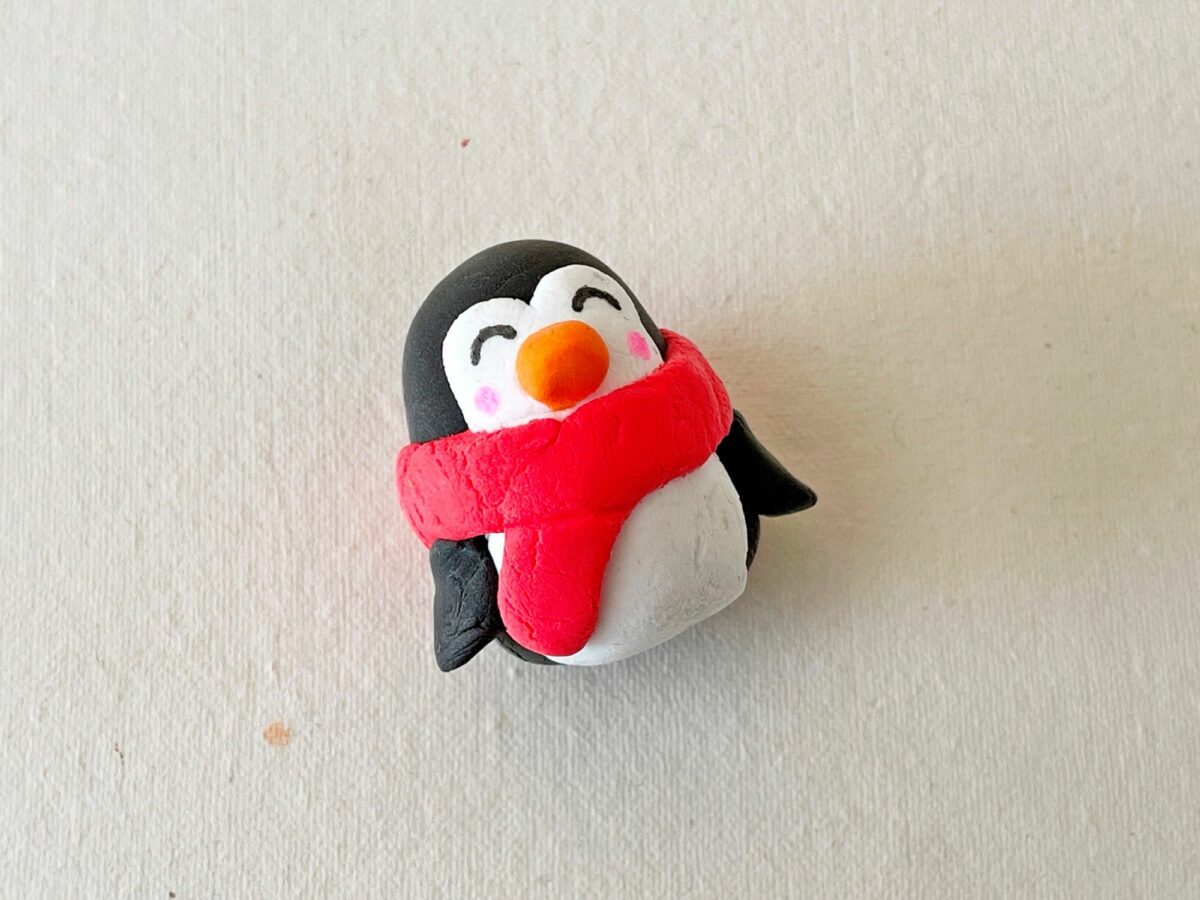 A penguin wearing a red scarf on a white surface.